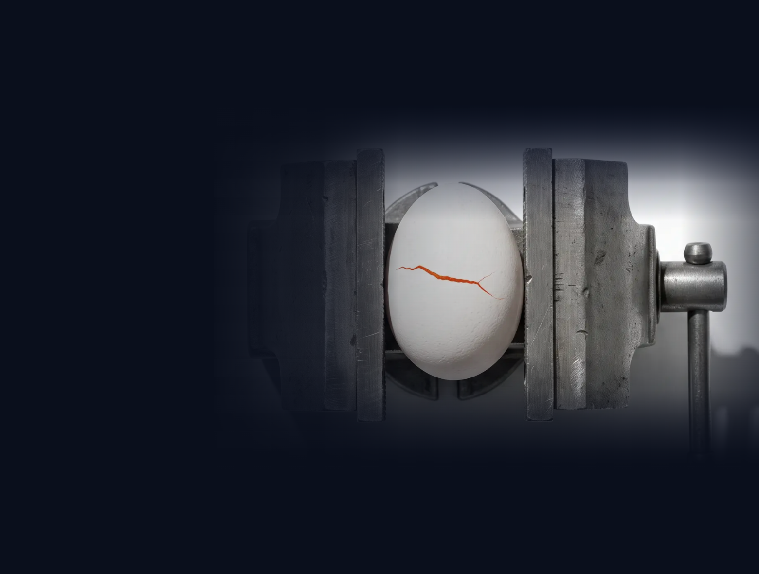 An egg held in a machinist's vise, a single hairline crack showing